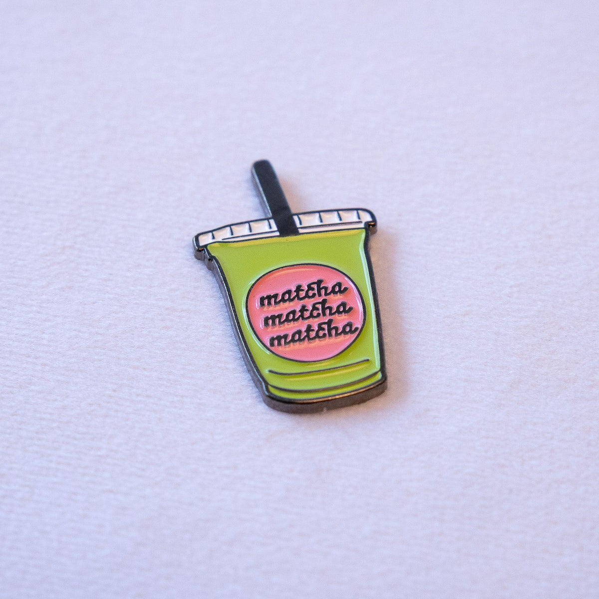 A green to-go cup with a black straw and a pink label reading matcha matcha matcha, seen from above.