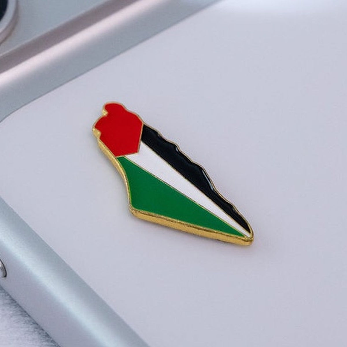 Gold-rimmed Palestine map silhouette pin, cropped lifestyle shot on the back of a phone