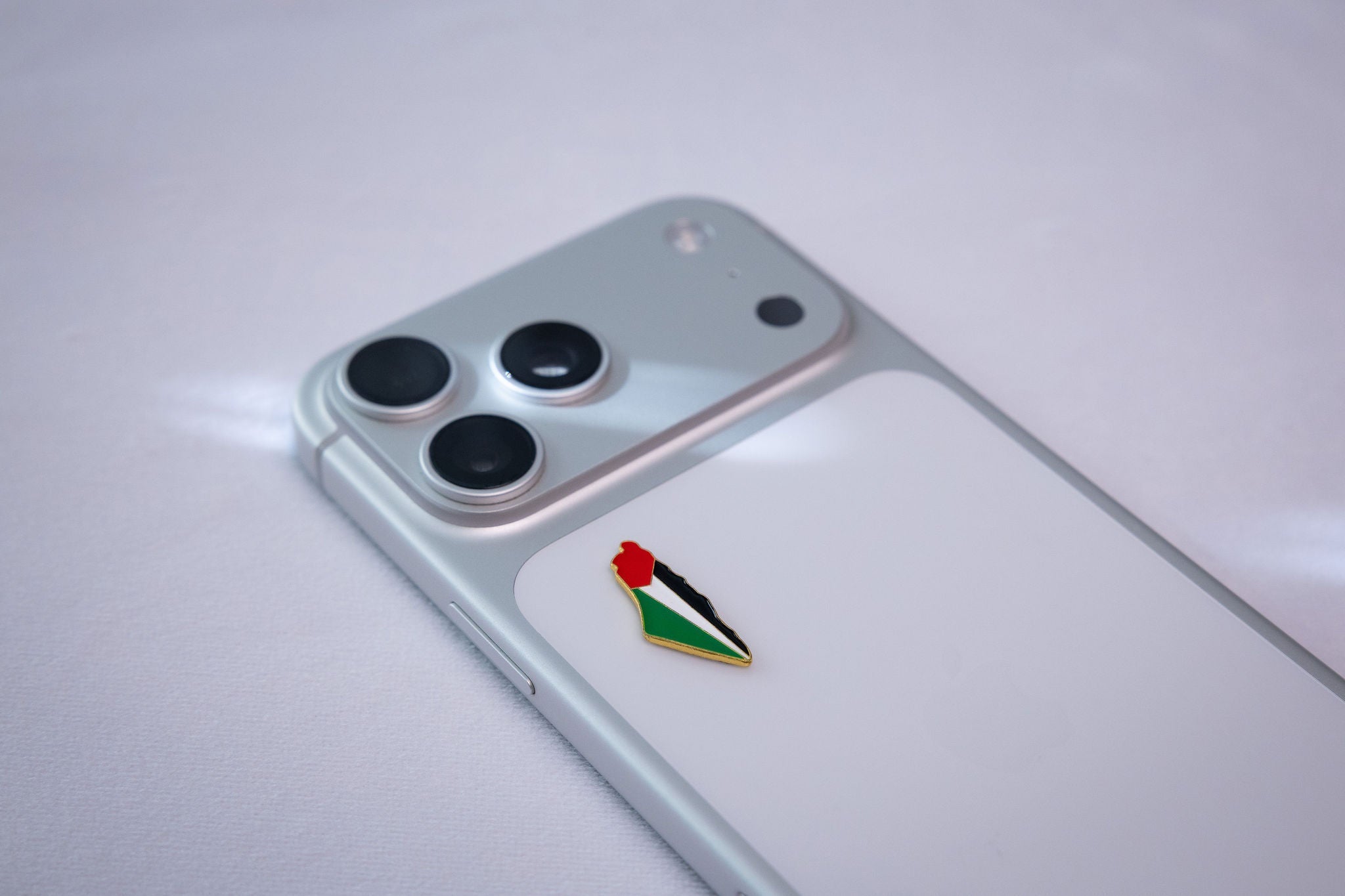 KAL-STK-0046 lifestyle shot — Palestine map-shape enamel pin on the back of a phone