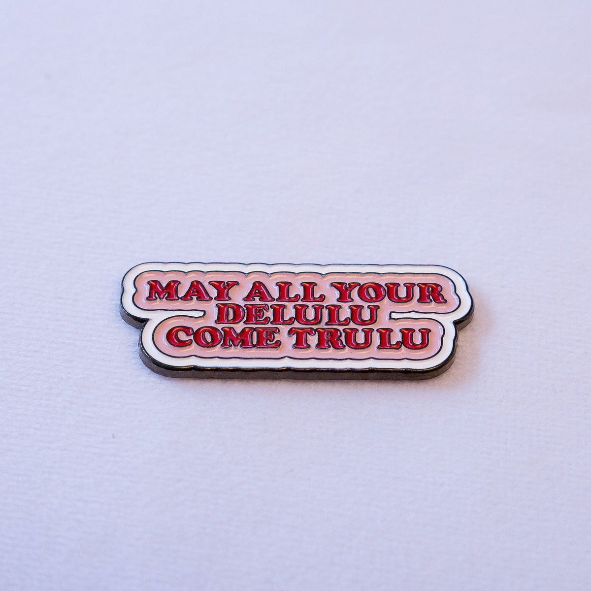 MAY ALL YOUR DELULU COME TRULU in bold red serif on a soft pink scalloped speech bubble.