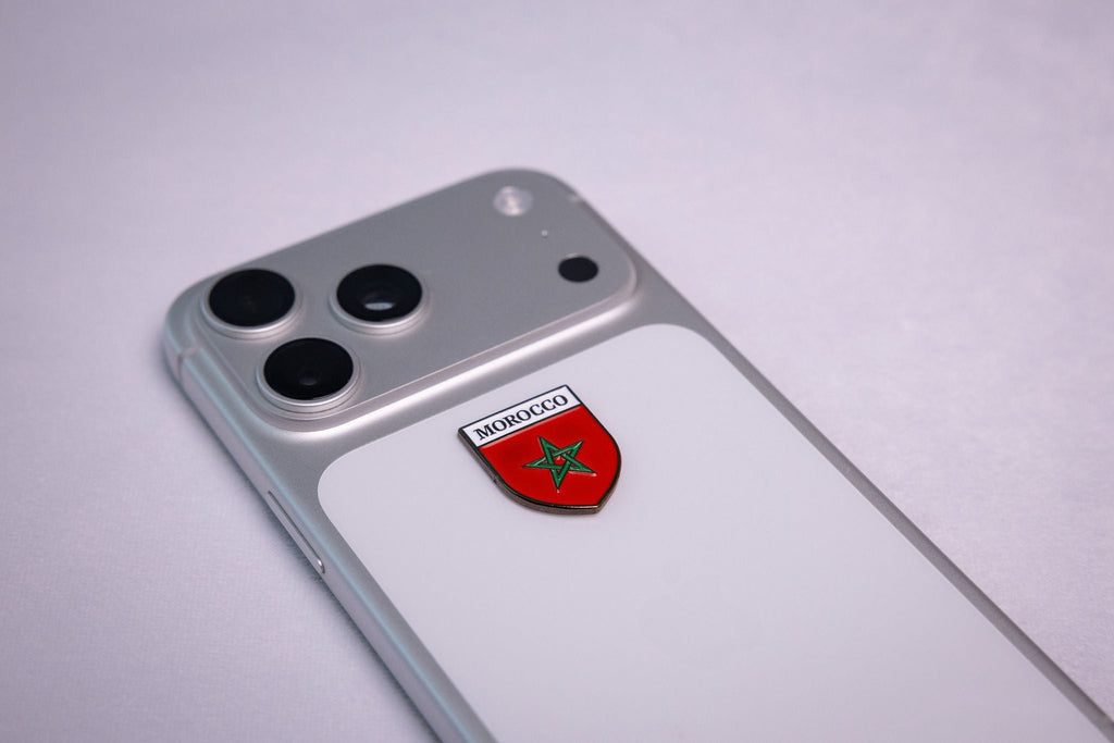 Red shield sticker reading MOROCCO with a green five-pointed star, applied to a phone case near the camera bump