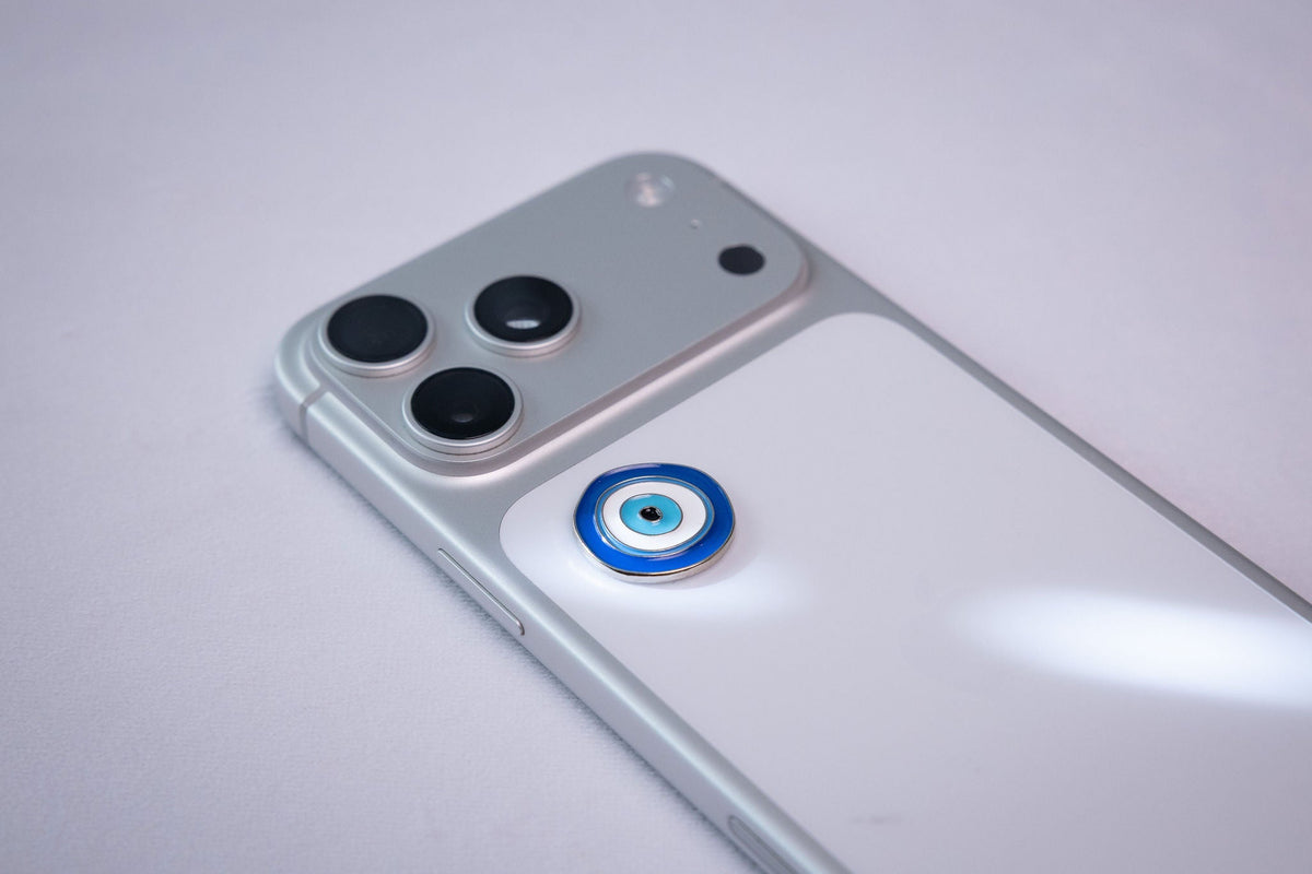Blue-and-white evil eye (nazar) amulet sticker, applied to a phone case near the camera bump