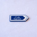 A blue highway sign cut as an arrow, بغداد above Baghdad, with a white chevron pointing the way.