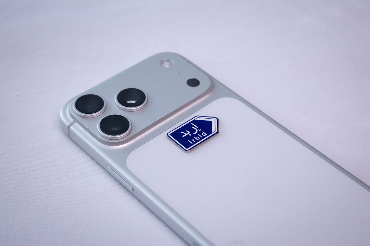 Blue Irbid (إربد) road-sign metal sticker, applied to a phone case near the camera bump