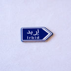 A blue highway sign cut as an arrow, إربد above Irbid.