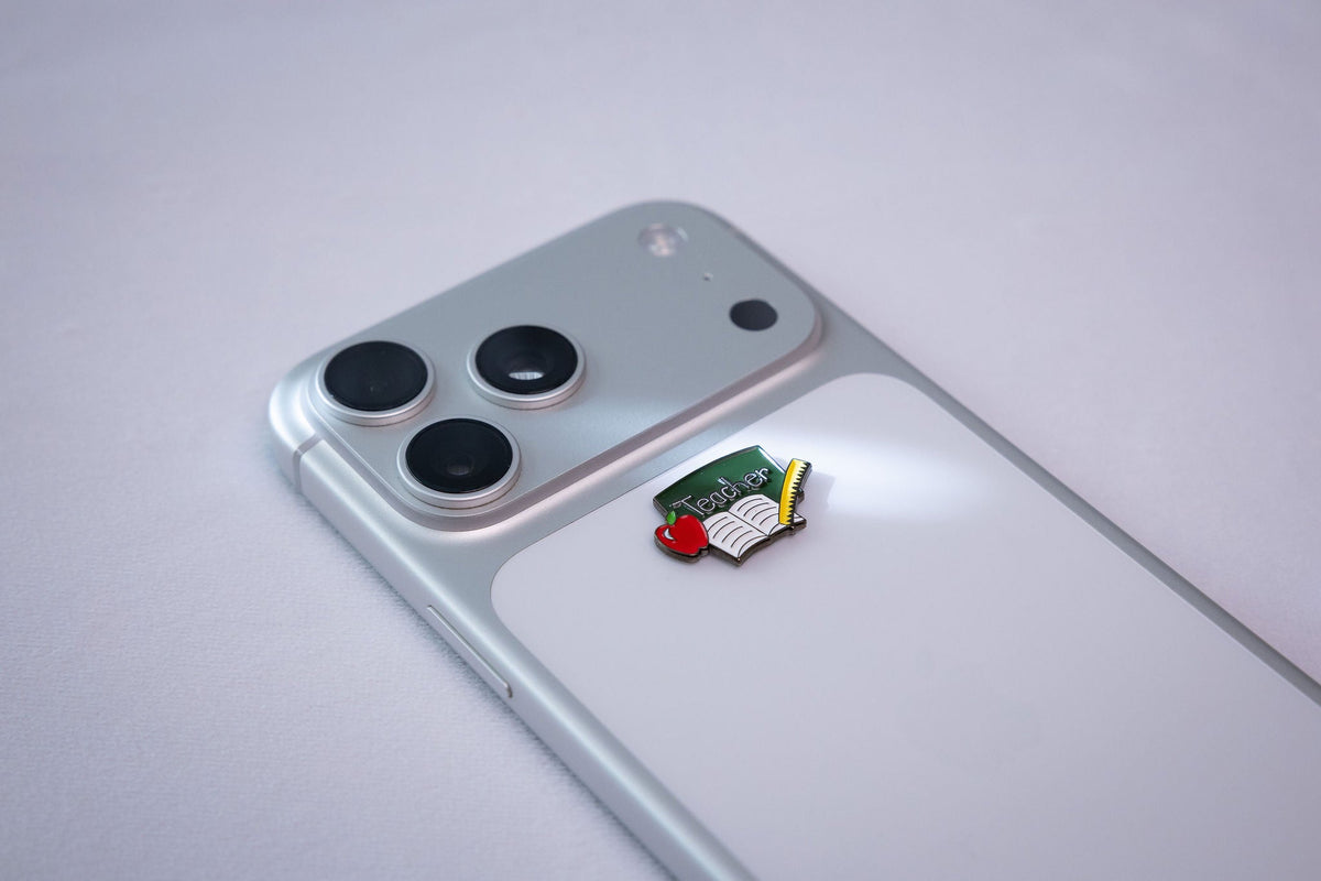 The Teacher chalkboard metal sticker applied to a phone case near the camera bump.