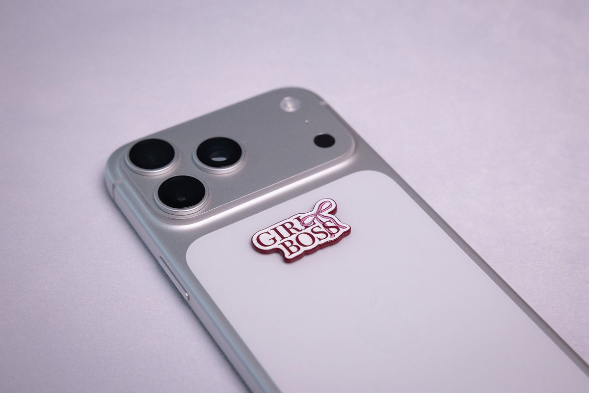 The GIRL BOSS metal sticker applied to a phone case near the camera bump.