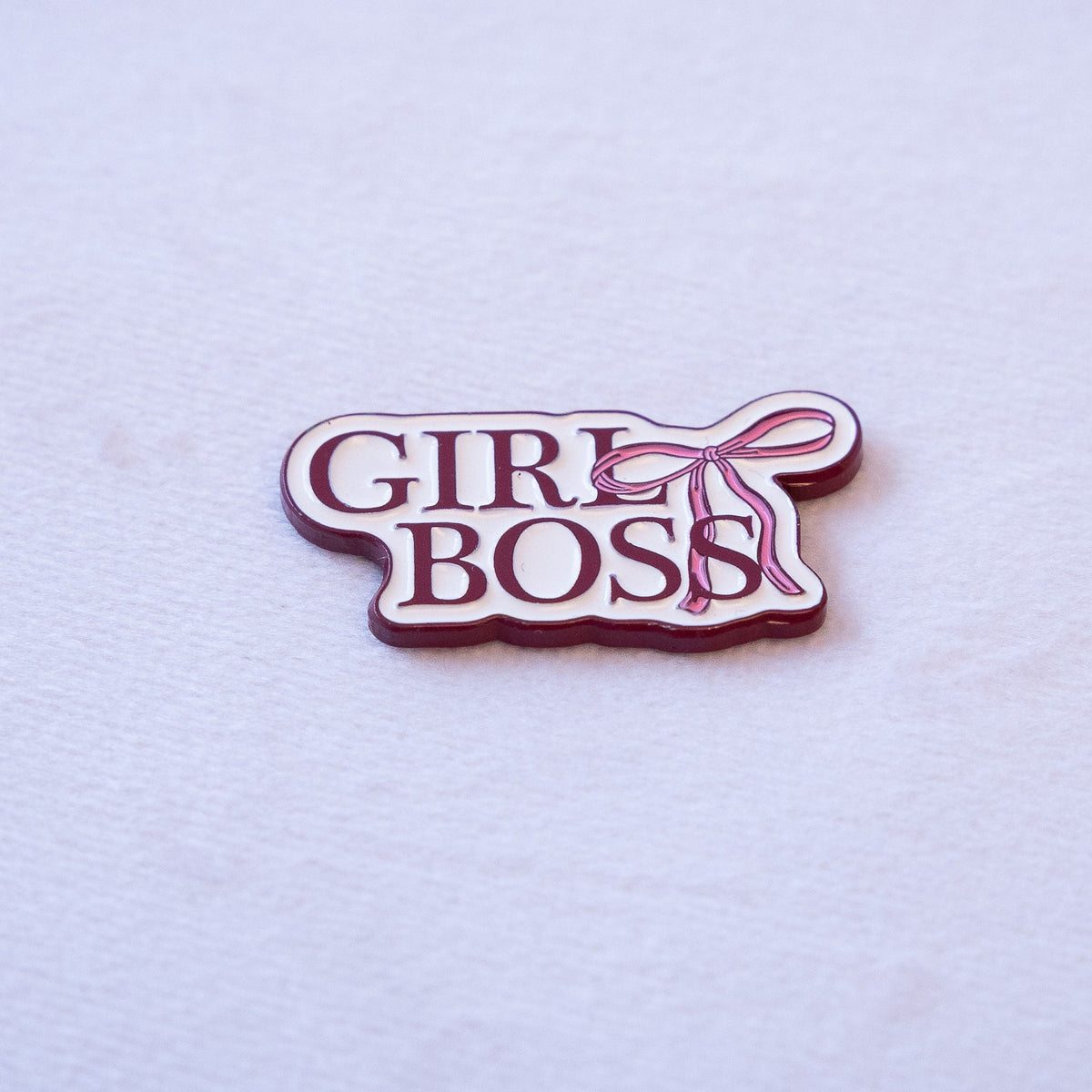 GIRL BOSS in burgundy serif capitals on two lines on a cream plate, with a pink bow trailing off the upper right, as a metal sticker.
