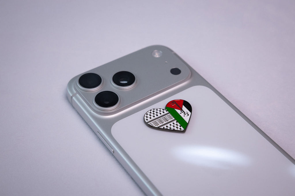 The Palestine keffiyeh heart metal sticker applied to a phone case near the camera bump.