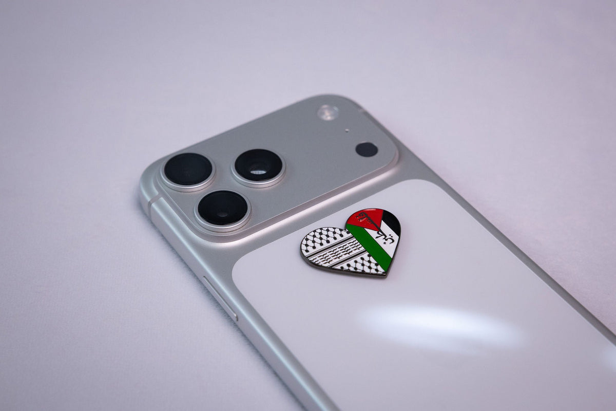 The Palestine keffiyeh heart metal sticker applied to a phone case near the camera bump.