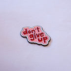 don't give up in red bubble letters on a pink cloud shape with a white outline, as a metal sticker.