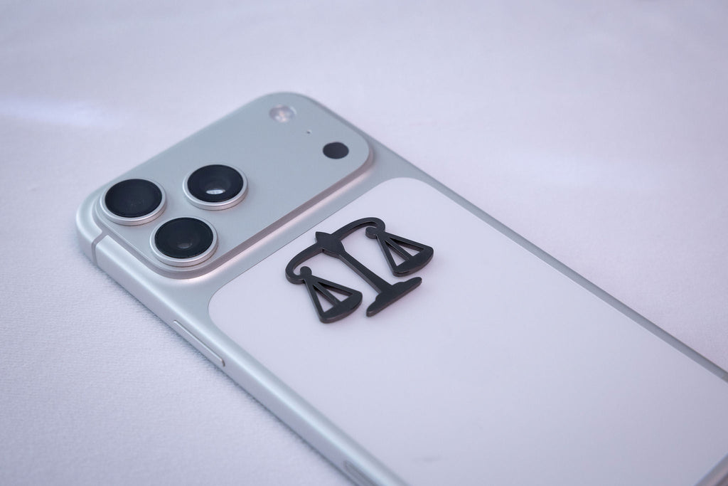 The scales of justice metal sticker applied to a phone case near the camera bump.