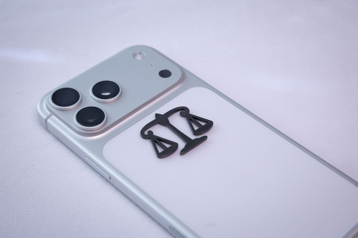 The scales of justice metal sticker applied to a phone case near the camera bump.
