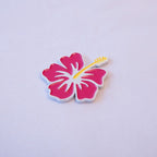 A magenta hibiscus with a yellow stamen and white outline, angled left on a pale background.