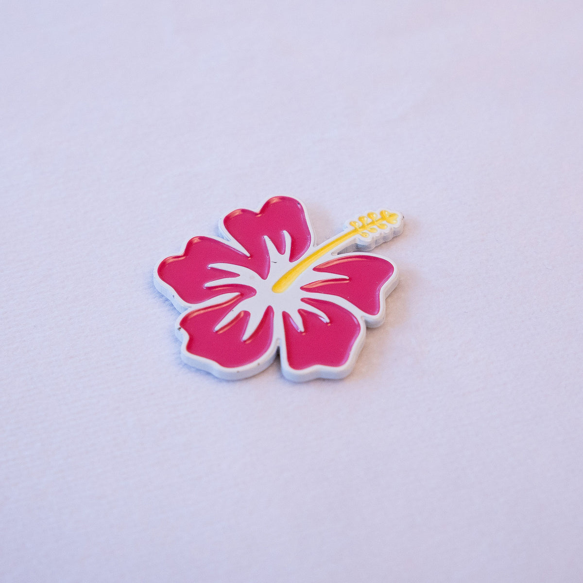 A magenta hibiscus with a yellow stamen and white outline, angled left on a pale background.