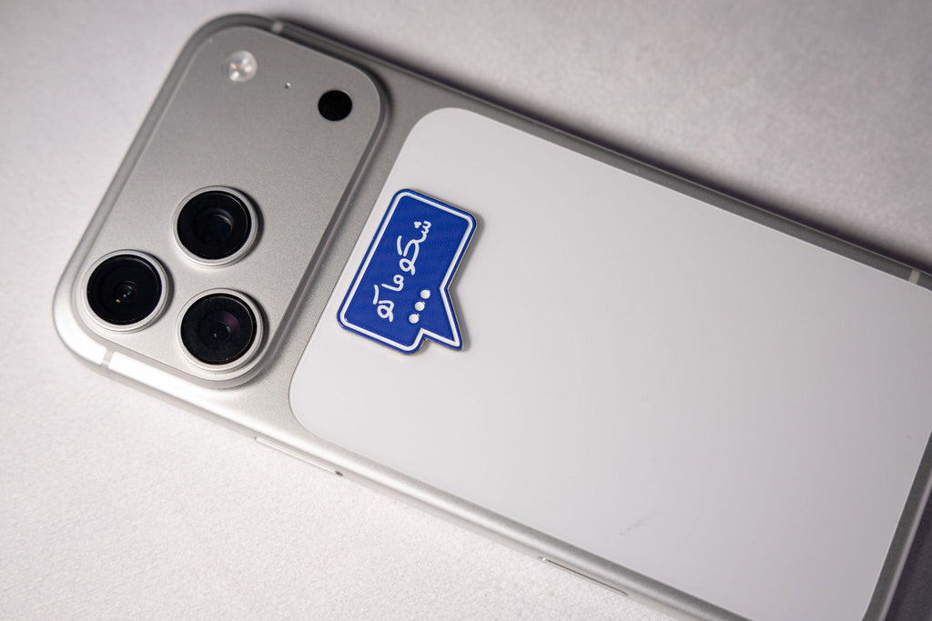 The Shku Maku (شكو ماكو) speech bubble metal sticker applied to a phone case near the camera bump.