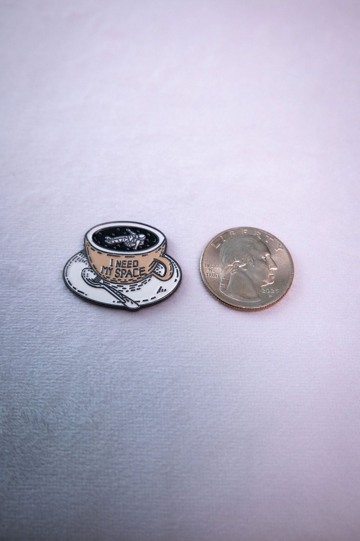 The I Need My Space astronaut teacup metal sticker beside a US quarter for scale.
