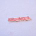 "i'm just a girl." in red letters with a cream outline, die-cut to the shape of the words, as a metal sticker.