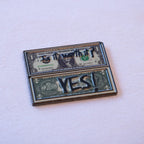 Two folded dollar bills stacked, "Is it worth it?" on the upper bill and "YES!" in bold caps across the lower one, as a metal sticker.