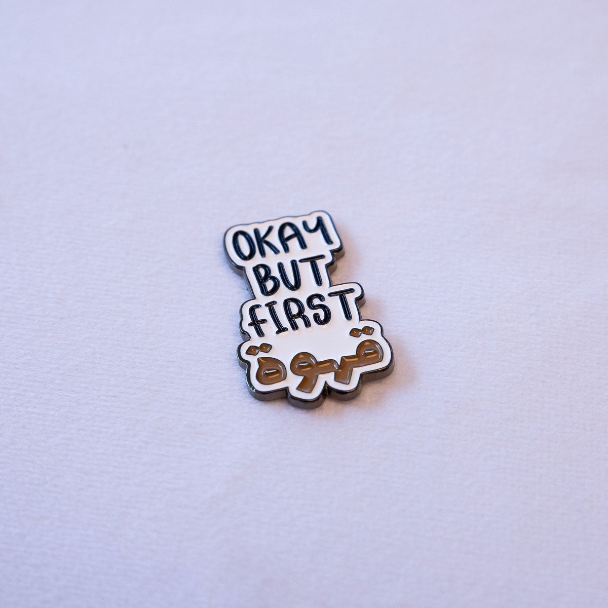 OKAY BUT FIRST in navy hand-lettered capitals with قهوة beneath it in warm brown, as a metal sticker.