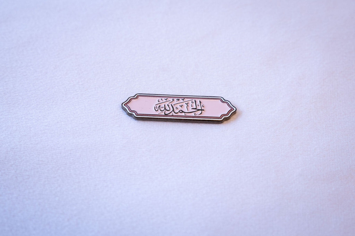 Alhamdulillah (الحمد لله) in black calligraphy on a soft pink scalloped-label sticker with a thin pink pinstripe border, flat lay on a light gray background